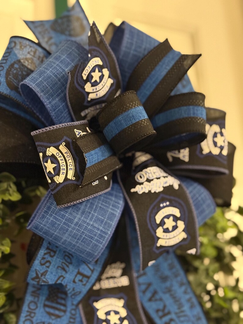 May include: A blue and black wreath with a police officer theme. The wreath is decorated with blue and black ribbon, and features a police badge with the words "Protect and Serve" and "Police Officer".