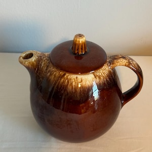 May include: A brown and white glazed ceramic teapot with a round body and a lid with a knob on top.