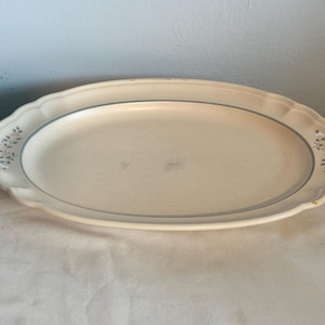 May include: An oval, off-white serving platter with a scalloped edge and a thin blue border. The platter has a floral design on the corners. The serving dish is made of ceramic and is suitable for serving food.