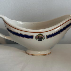 May include: White porcelain gravy boat with a blue and orange trim and a floral design.