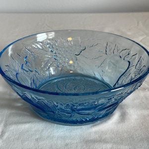 May include: A light blue glass bowl with a floral design. The bowl is made of clear glass with a blue tint and has a raised floral pattern.