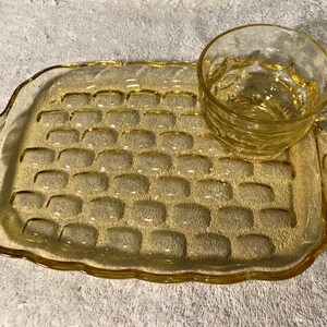 May include: A yellow glass serving tray with a raised, textured pattern and a matching yellow glass cup. The tray has a scalloped edge and two handles.