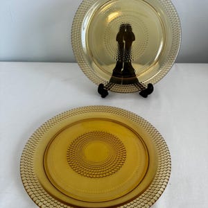 May include: Two amber glass dinner plates with a textured, raised pattern around the rim and a concentric circle pattern in the center.