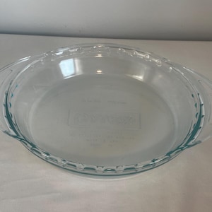 May include: A clear glass pie plate with two handles. The plate has a fluted edge and the words "Made in USA" are printed on the bottom.