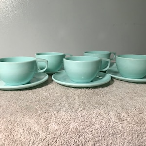 May include: Set of four light blue teacups and saucers. The cups and saucers are made of a smooth, glossy material.