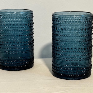 May include: Two blue glass tumblers with a textured, dotted surface. The glasses are empty and appear to be made of thick glass.