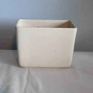 May include: A rectangular ceramic planter with a smooth, off-white finish and rounded corners. The vessel features a subtle, fine crackle glaze texture across its surface, with a wide, open top and a flat base, presenting a clean, simple form.