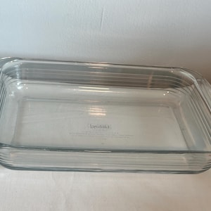 May include: A clear, rectangular glass baking dish with a ribbed design. The dish has rounded corners and a slightly raised rim. The brand name is visible on the bottom of the dish. Ideal for baking casseroles, desserts, and more.