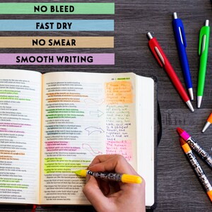May include: A close-up of an open Bible with highlighted verses and handwritten notes. The text includes verses from Proverbs 16:21 and 18:10. A hand is holding a yellow highlighter pen over the text. Several colorful pens are visible on a wooden surface.