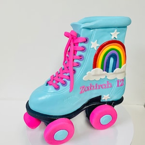 May include: A blue and pink roller skate cake decorated with a rainbow, clouds, and stars. The cake is personalized with the name "Zahirah" and the number "12".