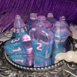 May include: A collection of handmade resin dice and potion bottle miniatures. The dice are blue and purple with white numbers. The potion bottles are clear with blue and purple glitter inside. The items are displayed on a decorative silver tray.