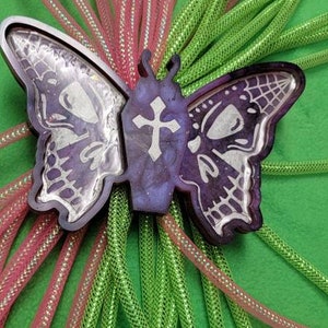 May include: A purple resin butterfly with a cross design, surrounded by pink and green sparkly mesh ribbon.