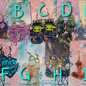 May include: Assortment of handmade resin earrings featuring various designs, including a glass dome with a rose, a potion bottle, a potted plant, a Stitch character, a shield, and a bottle with glitter.