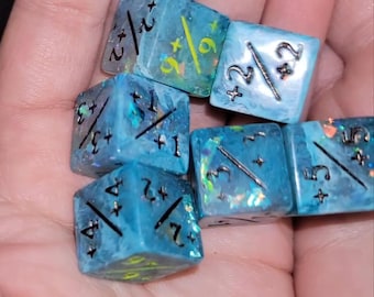 May include: Six blue and green dice with iridescent glitter. Each die has black numbers and symbols, including plus signs and fractions. The dice are in a hand.