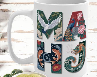 May include: A white ceramic mug featuring the letters MAHJ decorated with illustrations of a crane, a peacock, peonies, koi fish, and a dragon. The text LOVELY MAHJONG GIFT appears at the top. The mug is positioned behind a small plate of cookies.