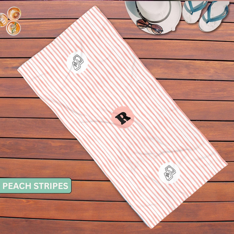 May include: A rectangular beach towel featuring a pattern of vertical peach-colored stripes on a white background. The towel includes a central circular emblem with the letter R and two smaller circular icons displaying a medical cross symbol.