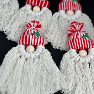May include: Five white yarn gnome ornaments with red and white striped hats and wooden bead noses. The hats have a candy cane and holly leaf design.
