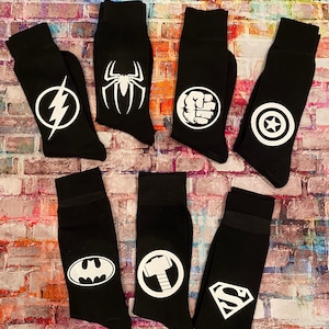 May include: Set of eight black socks with white superhero logos. The logos include: The Flash, Spiderman, Hulk, Captain America, Batman, Thor, Superman, and Iron Man.