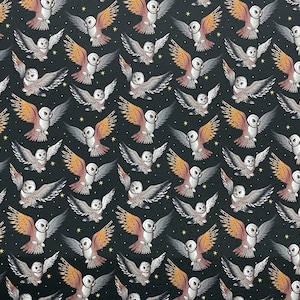 May include: A black fabric with a repeating pattern of white owls with orange and brown wings flying against a black background with yellow stars.