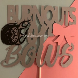 May include: A gray and pink cake topper with the text "Burnouts and Bows". The topper features a tire with flames and a pink bow.