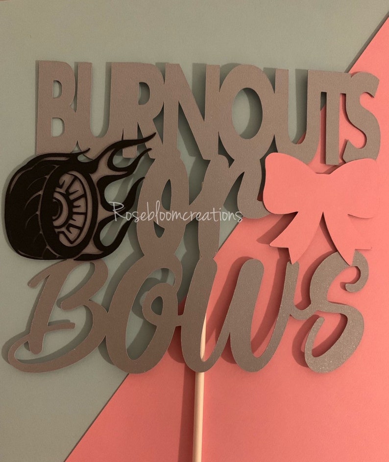 May include: A gray and pink cake topper with the text "Burnouts and Bows". The topper features a tire with flames and a pink bow.