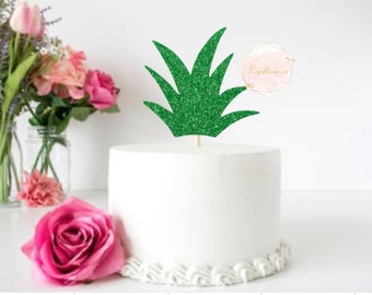 May include: Green glitter pineapple topper for a cake. The topper is made of green glitter cardstock and has a wooden stick for inserting into the cake.