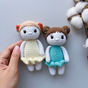 Puede incluir: Dos mu&ntilde;ecas de crochet con cuerpos blancos, cabello casta&ntilde;o y vestidos coloridos. La mu&ntilde;eca de la izquierda lleva un vestido amarillo y la mu&ntilde;eca de la derecha lleva un vestido azul.