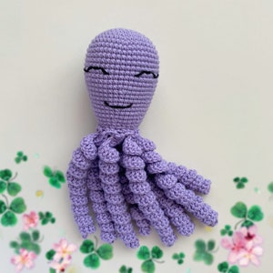 May include: A crocheted purple octopus with a smiling face. The octopus has eight tentacles and is made with a soft, textured yarn.