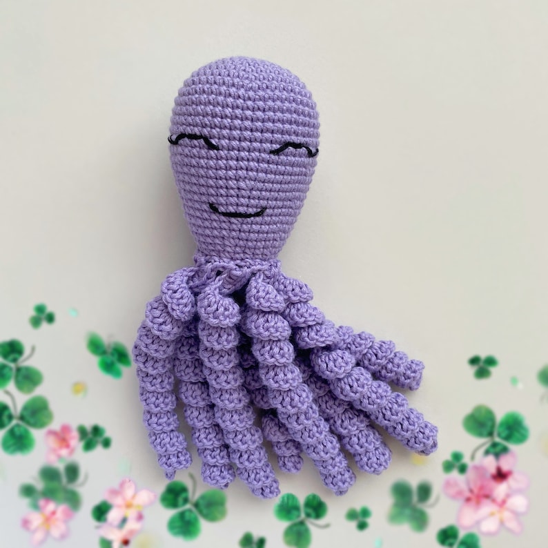 May include: A crocheted purple octopus with a smiling face. The octopus has eight tentacles and is made with a soft, textured yarn.