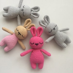 May include: Three crocheted bunny toys in different colors: gray, beige, and pink. Each bunny has a closed-eye expression and a simple stitched nose.