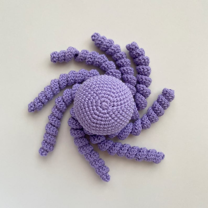 May include: A crocheted purple octopus toy with a round head and eight long, curled tentacles.