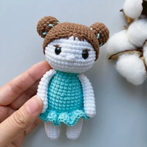 Puede incluir: Una mu&ntilde;eca de crochet con cabello marr&oacute;n, piel blanca y un vestido turquesa. La mu&ntilde;eca tiene ojos negros y una peque&ntilde;a nariz de crochet.