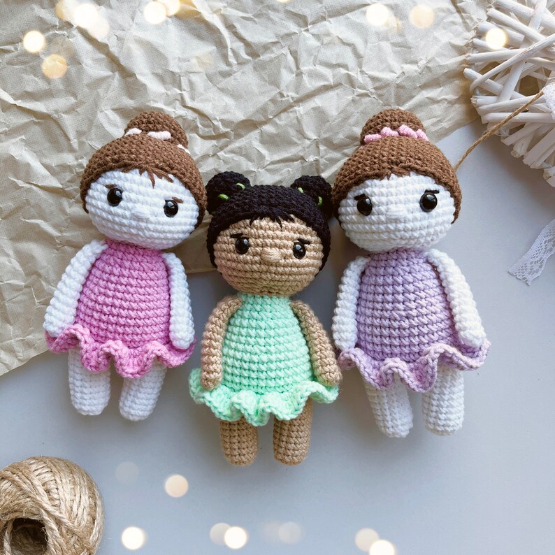 Puede incluir: Tres mu&ntilde;ecas de crochet con vestidos de diferentes colores. Las mu&ntilde;ecas tienen el pelo casta&ntilde;o y caras blancas con ojos negros. Los vestidos son rosa, verde y morado.