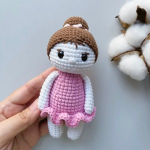 Puede incluir: Una mu&ntilde;eca de crochet con el pelo marr&oacute;n en un mo&ntilde;o, que lleva un vestido rosa. La mu&ntilde;eca tiene la piel blanca y los ojos negros.