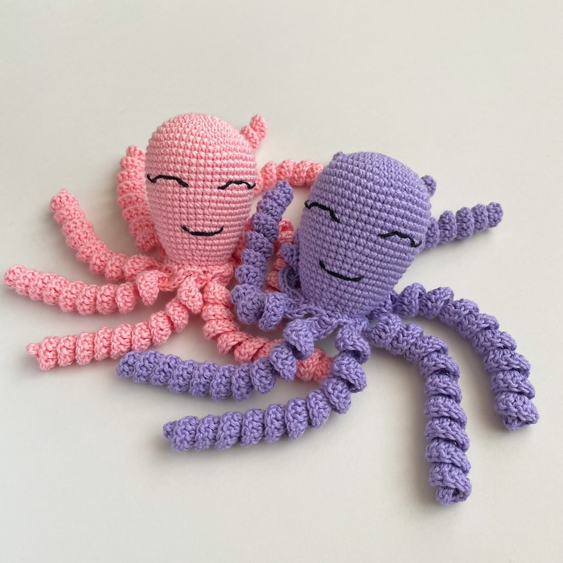 May include: Two crocheted octopus plushies, one pink and one purple, with smiling faces. The octopus plushies have eight tentacles each.