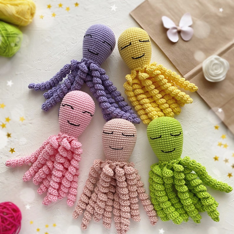 May include: Five crocheted octopus plushies in different colors: purple, yellow, pink, light pink, and green. Each octopus has a smiling face with embroidered eyes.