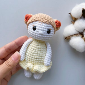Puede incluir: Una mu&ntilde;eca de crochet con un vestido amarillo y lazos de pelo naranja. La mu&ntilde;eca tiene ojos negros y una cara blanca.