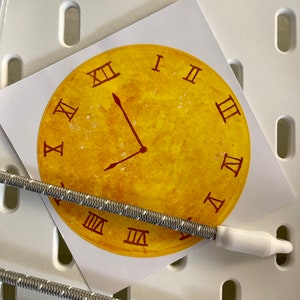 May include: A yellow clock face with Roman numerals and a single hand pointing to the 4 o'clock position. The clock face is on a white background.