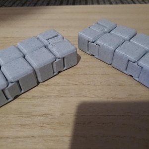 May include: Two grey fidget toys made of small connected cubes. Each toy has a textured surface.