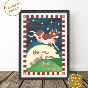 May include: Framed print featuring a whimsical illustration of a brown and white cow leaping over a yellow moon. The artwork includes stars, a green hill, and the text "the cow jumped over the moon" in pink script, set against a dark blue background.