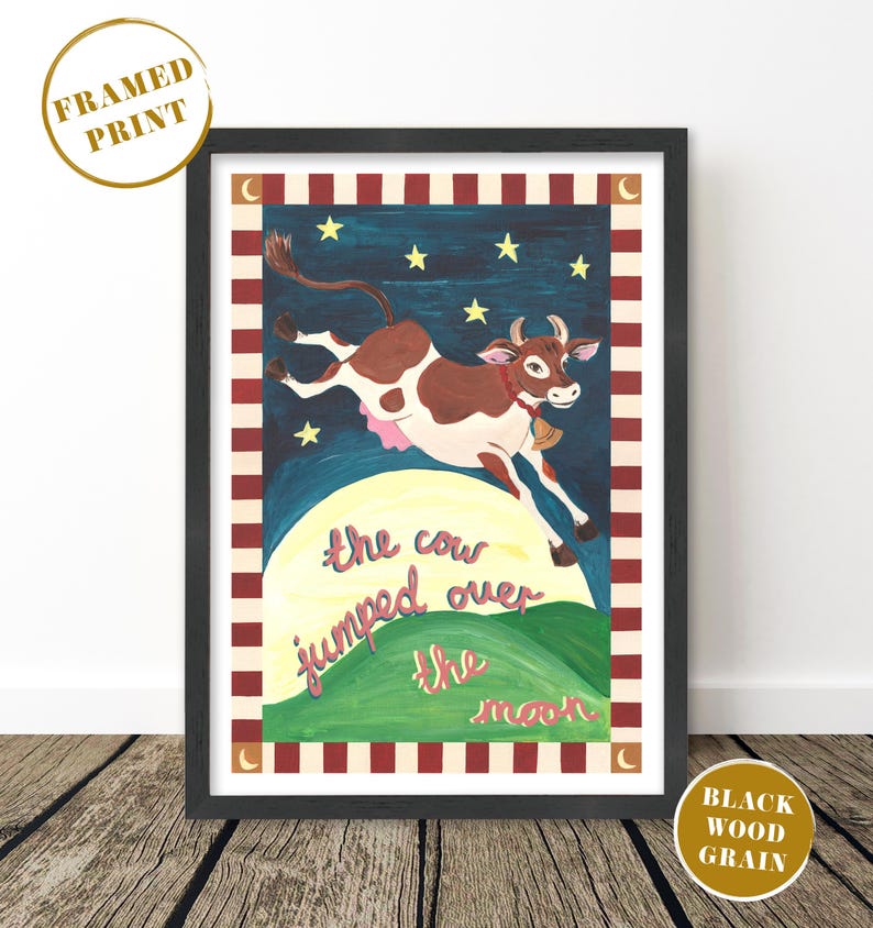 May include: Framed print featuring a whimsical illustration of a brown and white cow leaping over a yellow moon. The artwork includes stars, a green hill, and the text "the cow jumped over the moon" in pink script, set against a dark blue background.