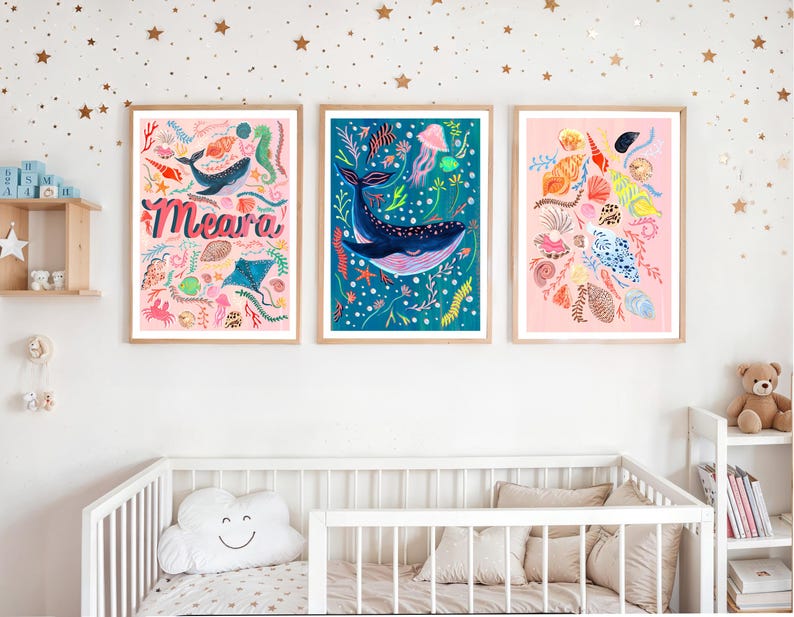 May include: Three framed wall art prints featuring marine life. The left print has a pink background with the name Meara, a whale, and seashells. The center print shows a blue background with a large whale and jellyfish. The right print displays seashells.