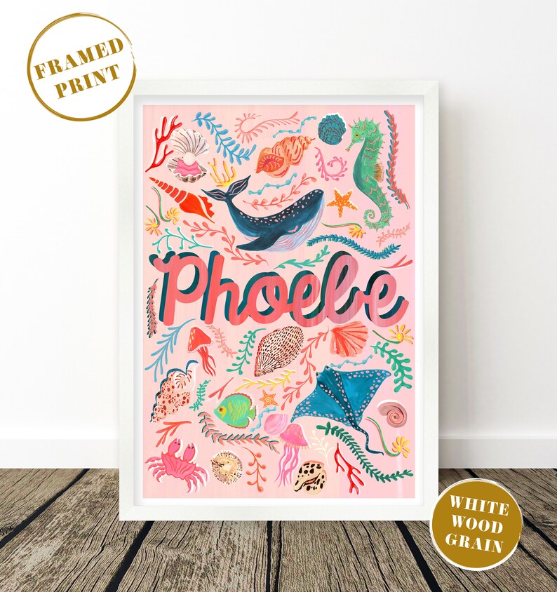 May include: A framed print in a white wood grain frame featuring a pink background with the name Phoebe in large letters. The artwork displays various colorful marine life including a whale, seahorse, stingray, crab, jellyfish, and seashells.