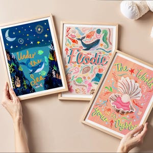 May include: Three framed art prints featuring marine themes. One print shows a whale in a dark blue ocean with the text Under the Sea. Another displays the name Elodie with sea creatures. The third shows an open oyster with the text The World is your Oyster.