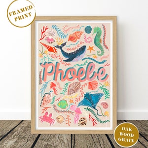 May include: A framed print in an oak wood grain frame featuring a light beige background with a colorful illustration of a whale, seahorse, stingray, crab, fish, jellyfish, and various seashells and coral, with the name Phoebe in pink text.