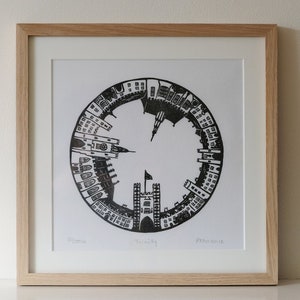 May include: Black and white print of a circular design depicting the buildings of Trinity College, Dublin. The print is framed in a light wood frame. The text "Trinity" is printed below the design.