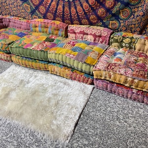 May include: A patchwork floor sofa with multiple cushions in various colors, including pink, yellow, green, and red. The cushions have a quilted design. A white, fluffy rug is in front of the sofa.
