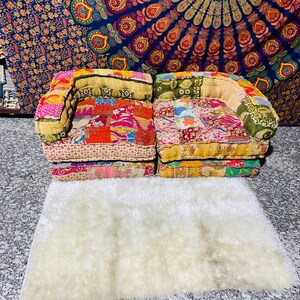 Puede incluir: Dos pequeños sofás patchwork coloridos con reposabrazos redondeados se asientan sobre una alfombra blanca y esponjosa. Los sofás presentan una variedad de patrones de tela en tonos de rojo, rosa, amarillo y verde. Una vibrante tapicería con un diseño de mandala cuelga en el fondo.