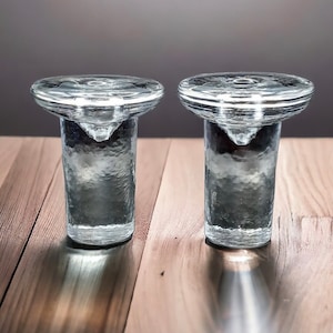 Puede incluir: Dos candelabros de vidrio transparente con superficie texturizada. Los candelabros tienen una parte superior ancha y plana y una base estrecha.