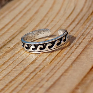 May include: Silver toe ring with a wave design. The ring is open and adjustable.
